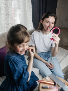 Kız, annesinin yüzüne makyaj yapar ve oynaşır. Bakıcı ebeveyn çocuğunun yüzünü boyamasına izin verir. Mutlu bir çocukluk. Sevgi dolu bir aile ve eğlence anlayışı. Küçük kız makyajını yapıyor.