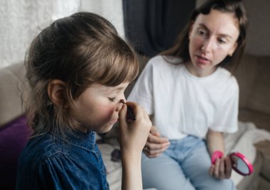 Kız, annesinin yüzüne makyaj yapar ve oynaşır. Bakıcı ebeveyn çocuğunun yüzünü boyamasına izin verir. Mutlu bir çocukluk. Sevgi dolu bir aile ve eğlence anlayışı. Küçük kız makyajını yapıyor.