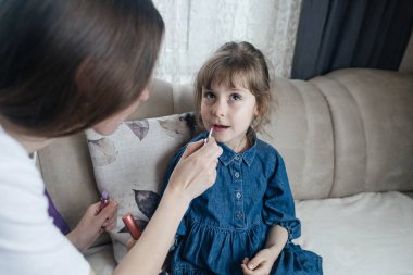Anne kızının yüzüne makyaj yapıyor ve birlikte takılıyorlar. Ailedeki kadınlar arasındaki iletişim. Eğlence zamanı. Mutlu aile kavramı. Küçük kız makyajını yapıyor.