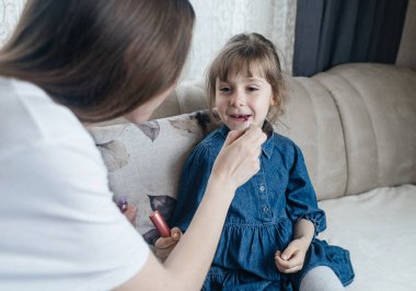 Anne kızının yüzüne makyaj yapıyor ve birlikte takılıyorlar. Ailedeki kadınlar arasındaki iletişim. Eğlence zamanı. Mutlu aile kavramı. Küçük kız makyajını yapıyor.