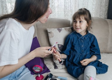 Anne kızının yüzüne makyaj yapıyor ve birlikte takılıyorlar. Ailedeki kadınlar arasındaki iletişim. Eğlence zamanı. Mutlu aile kavramı. Küçük kız makyajını yapıyor.