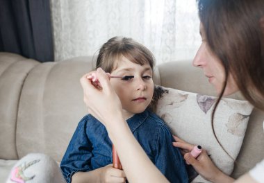 Anne kızının yüzüne makyaj yapıyor ve birlikte takılıyorlar. Ailedeki kadınlar arasındaki iletişim. Eğlence zamanı. Mutlu aile kavramı. Küçük kız makyajını yapıyor.