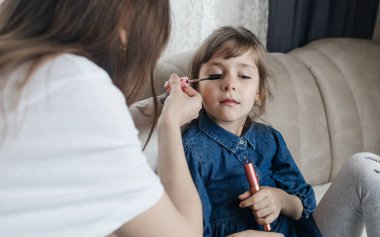Anne kızının yüzüne makyaj yapıyor ve birlikte takılıyorlar. Ailedeki kadınlar arasındaki iletişim. Eğlence zamanı. Mutlu aile kavramı. Küçük kız makyajını yapıyor.