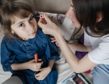 Anne kızının yüzüne makyaj yapıyor ve birlikte takılıyorlar. Ailedeki kadınlar arasındaki iletişim. Eğlence zamanı. Mutlu aile kavramı. Küçük kız makyajını yapıyor.