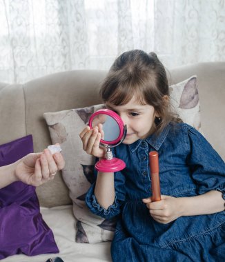 Anne kızının yüzüne makyaj yapıyor ve birlikte takılıyorlar. Ailedeki kadınlar arasındaki iletişim. Eğlence zamanı. Mutlu aile kavramı. Küçük kız makyajını yapıyor.