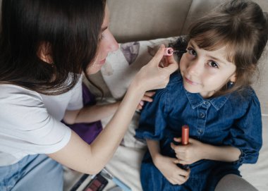 Anne kızının yüzüne makyaj yapıyor ve birlikte takılıyorlar. Ailedeki kadınlar arasındaki iletişim. Eğlence zamanı. Mutlu aile kavramı. Küçük kız makyajını yapıyor.