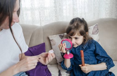 Anne kızının yüzüne makyaj yapıyor ve birlikte takılıyorlar. Ailedeki kadınlar arasındaki iletişim. Eğlence zamanı. Mutlu aile kavramı. Küçük kız makyajını yapıyor.
