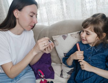 Anne kızının yüzüne makyaj yapıyor ve birlikte takılıyorlar. Ailedeki kadınlar arasındaki iletişim. Eğlence zamanı. Mutlu aile kavramı. Küçük kız makyajını yapıyor.