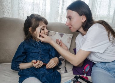 Anne kızının yüzüne makyaj yapıyor ve birlikte takılıyorlar. Ailedeki kadınlar arasındaki iletişim. Eğlence zamanı. Mutlu aile kavramı. Küçük kız makyajını yapıyor.