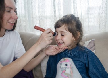 Anne kızının yüzüne makyaj yapıyor ve birlikte takılıyorlar. Ailedeki kadınlar arasındaki iletişim. Eğlence zamanı. Mutlu aile kavramı. Küçük kız makyajını yapıyor.