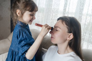 Kız, annesinin yüzüne makyaj yapar ve oynaşır. Bakıcı ebeveyn çocuğunun yüzünü boyamasına izin verir. Mutlu bir çocukluk. Sevgi dolu bir aile ve eğlence anlayışı. Küçük kız makyajını yapıyor.