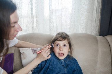 Anne kızının yüzüne makyaj yapıyor ve birlikte takılıyorlar. Ailedeki kadınlar arasındaki iletişim. Eğlence zamanı. Mutlu aile kavramı. Küçük kız makyajını yapıyor.