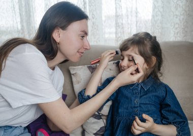 Anne kızının yüzüne makyaj yapıyor ve birlikte takılıyorlar. Ailedeki kadınlar arasındaki iletişim. Eğlence zamanı. Mutlu aile kavramı. Küçük kız makyajını yapıyor.