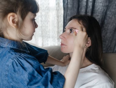 Kız, annesinin yüzüne makyaj yapar ve oynaşır. Bakıcı ebeveyn çocuğunun yüzünü boyamasına izin verir. Mutlu bir çocukluk. Sevgi dolu bir aile ve eğlence anlayışı. Küçük kız makyajını yapıyor.