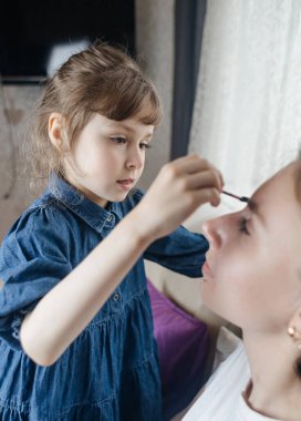 Kız, annesinin yüzüne makyaj yapar ve oynaşır. Bakıcı ebeveyn çocuğunun yüzünü boyamasına izin verir. Mutlu bir çocukluk. Sevgi dolu bir aile ve eğlence anlayışı. Küçük kız makyajını yapıyor.