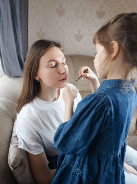 Kız, annesinin yüzüne makyaj yapar ve oynaşır. Bakıcı ebeveyn çocuğunun yüzünü boyamasına izin verir. Mutlu bir çocukluk. Sevgi dolu bir aile ve eğlence anlayışı. Küçük kız makyajını yapıyor.