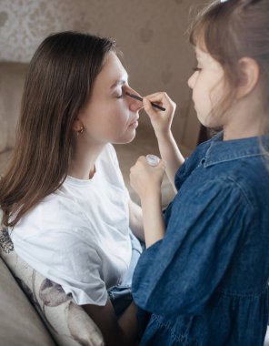 Kız, annesinin yüzüne makyaj yapar ve oynaşır. Bakıcı ebeveyn çocuğunun yüzünü boyamasına izin verir. Mutlu bir çocukluk. Sevgi dolu bir aile ve eğlence anlayışı. Küçük kız makyajını yapıyor.