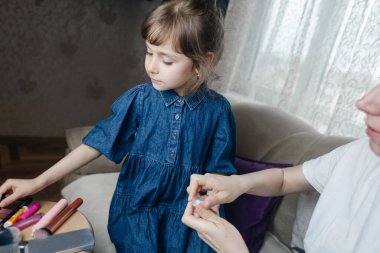 Kız, annesinin yüzüne makyaj yapar ve oynaşır. Bakıcı ebeveyn çocuğunun yüzünü boyamasına izin verir. Mutlu bir çocukluk. Sevgi dolu bir aile ve eğlence anlayışı. Küçük kız makyajını yapıyor.