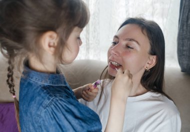 Kız, annesinin yüzüne makyaj yapar ve oynaşır. Bakıcı ebeveyn çocuğunun yüzünü boyamasına izin verir. Mutlu bir çocukluk. Sevgi dolu bir aile ve eğlence anlayışı. Küçük kız makyajını yapıyor.