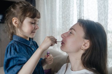 Kız, annesinin yüzüne makyaj yapar ve oynaşır. Bakıcı ebeveyn çocuğunun yüzünü boyamasına izin verir. Mutlu bir çocukluk. Sevgi dolu bir aile ve eğlence anlayışı. Küçük kız makyajını yapıyor.