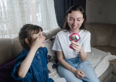 Kız, annesinin yüzüne makyaj yapar ve oynaşır. Bakıcı ebeveyn çocuğunun yüzünü boyamasına izin verir. Mutlu bir çocukluk. Sevgi dolu bir aile ve eğlence anlayışı. Küçük kız makyajını yapıyor.