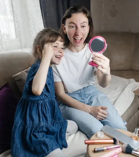 Kız, annesinin yüzüne makyaj yapar ve oynaşır. Bakıcı ebeveyn çocuğunun yüzünü boyamasına izin verir. Mutlu bir çocukluk. Sevgi dolu bir aile ve eğlence anlayışı. Küçük kız makyajını yapıyor.