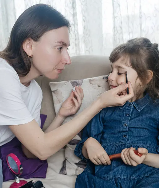 Anne kızının yüzüne makyaj yapıyor ve birlikte takılıyorlar. Ailedeki kadınlar arasındaki iletişim. Eğlence zamanı. Mutlu aile kavramı. Küçük kız makyajını yapıyor.