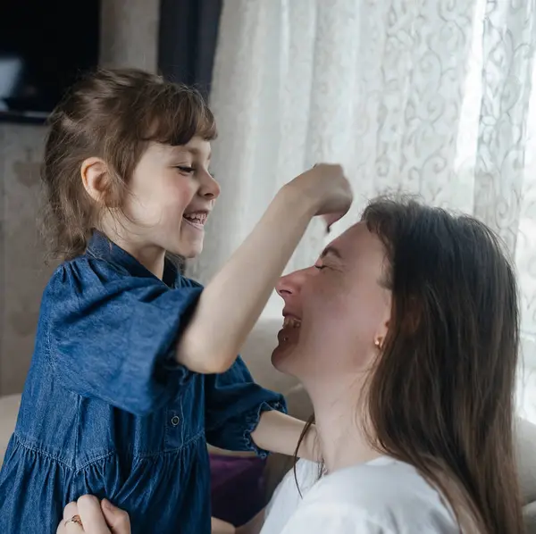 Kız, annesinin yüzüne makyaj yapar ve oynaşır. Bakıcı ebeveyn çocuğunun yüzünü boyamasına izin verir. Mutlu bir çocukluk. Sevgi dolu bir aile ve eğlence anlayışı. Küçük kız makyajını yapıyor.