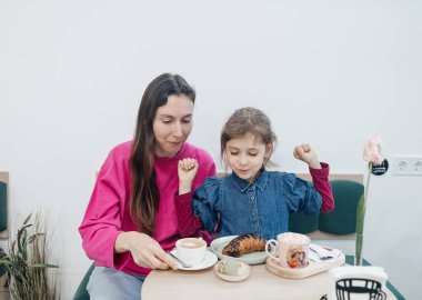 Anne ve kızı bir kafede, kahve ve kakao içiyor, kruvasan ve kek yiyor. Eğleniyoruz ve birlikte vakit geçiriyoruz.