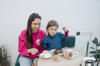 Anne ve kızı bir kafede, kahve ve kakao içiyor, kruvasan ve kek yiyor. Eğleniyoruz ve birlikte vakit geçiriyoruz.