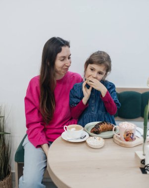 Anne ve kızı bir kafede, kahve ve kakao içiyor, kruvasan ve kek yiyor. Eğleniyoruz ve birlikte vakit geçiriyoruz.