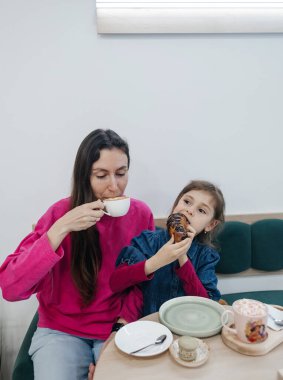Anne ve kızı bir kafede, kahve ve kakao içiyor, kruvasan ve kek yiyor. Eğleniyoruz ve birlikte vakit geçiriyoruz.