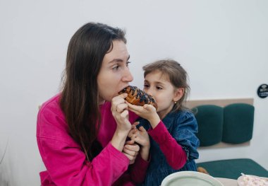 Anne ve kızı bir kafede, kahve ve kakao içiyor, kruvasan ve kek yiyor. Eğleniyoruz ve birlikte vakit geçiriyoruz.