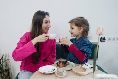 Anne ve kızı bir kafede, kahve ve kakao içiyor, kruvasan ve kek yiyor. Eğleniyoruz ve birlikte vakit geçiriyoruz.