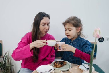 Anne ve kızı bir kafede, kahve ve kakao içiyor, kruvasan ve kek yiyor. Eğleniyoruz ve birlikte vakit geçiriyoruz.