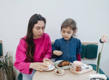 Anne ve kızı bir kafede, kahve ve kakao içiyor, kruvasan ve kek yiyor. Eğleniyoruz ve birlikte vakit geçiriyoruz.