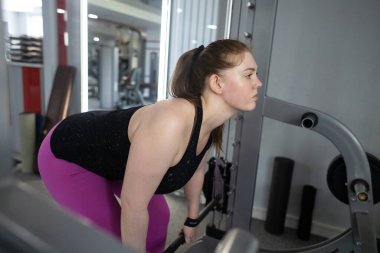 Ayrıca Smith Machine üzerinde egzersiz yapan cüsseli bir kadın. Halterle simülatöre çömelmiş. Kilo kaybı için egzersiz