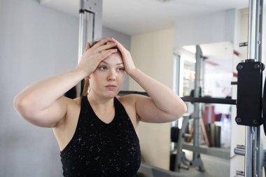 Ayrıca Smith Machine üzerinde egzersiz yapan cüsseli bir kadın. Halterle simülatöre çömelmiş. Kilo kaybı için egzersiz