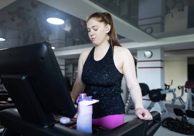 Spor salonunda koşu bandında çalışan normal vücutlu gerçek bir kadın. Gerçekçi zindelik ve sağlıklı kilo verme motivasyonu