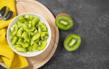 Kiwifruit taze yaz salatası dilimlenmiş yeşil kivi ile beyaz bir kâse üzerinde tahta kesme tahtası üzerinde koyu gri masa manzaralı fotokopi alanı ile.