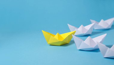 Leadership business concept with a yellow leader paper boat leading among white ones on blue background with copy space. clipart