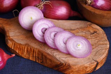 Dilimlenmiş Tropea kırmızı soğanını ahşap kesim tahtasına koy ve arka planda bütün kırmızı soğanları..