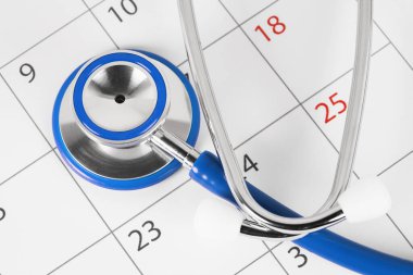 Takvim sayfasında steteskopun yakın plan görüntüsü, doktor randevusu planlama ve sağlık kontrolleri.