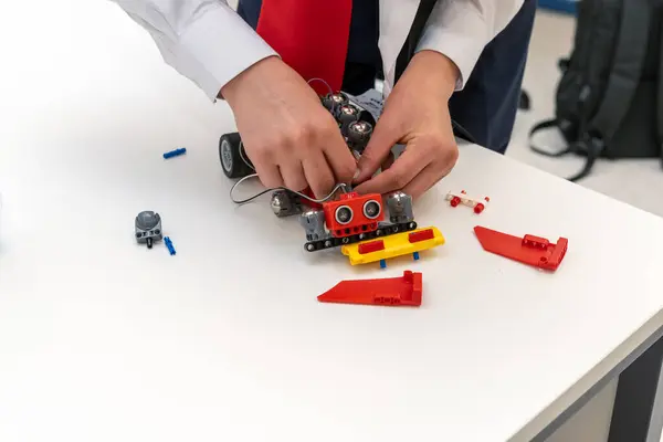 Öğrenci masanın üzerinde kırmızı bir inşaat setinden bir robot monte ediyor.