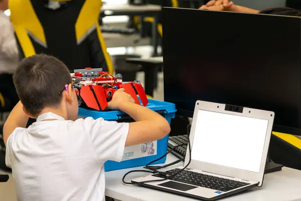 Çocuk masada oturmuş robotunu test ediyor ve programlıyor.