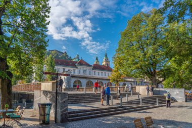 LJUBJANA, SLOVENIA - NOVEMBER 05.2022: Merkez marketin yanındaki köprüde bulunan insanlarla sokak görüntüsü, Katedral Kulesi 'nin arka planı