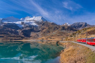 OSPIZIO BERNINA, SWitzERLAND - 28 Ekim 2022: Rhaetian 'ın Bernina Ekspresi' nde Bianco Gölü demiryolu hattı, arka plan güzel dağ