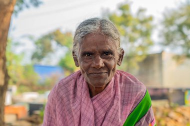 Puttaparthi, India - January 21.2023: Indian old lady close up looking in the camera at a vegetable market in Puttaparthi