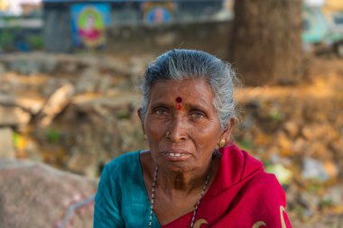 Puttaparthi, India - January 21.2023: Indian old lady with gray hair, close up, looking in the camera at a vegetable market in Puttaparthi