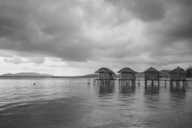 Saporkren, Waisai Adası, Raja Ampat sahillerindeki yıkılmış su evleri, arka plan bulutlu gökyüzü, siyah beyaz